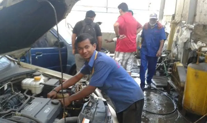 Friendly workshop technician performing engine maintenance check under the hood.