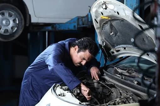 Focused senior technician in blue coveralls performing precise engine tuning and servicing.